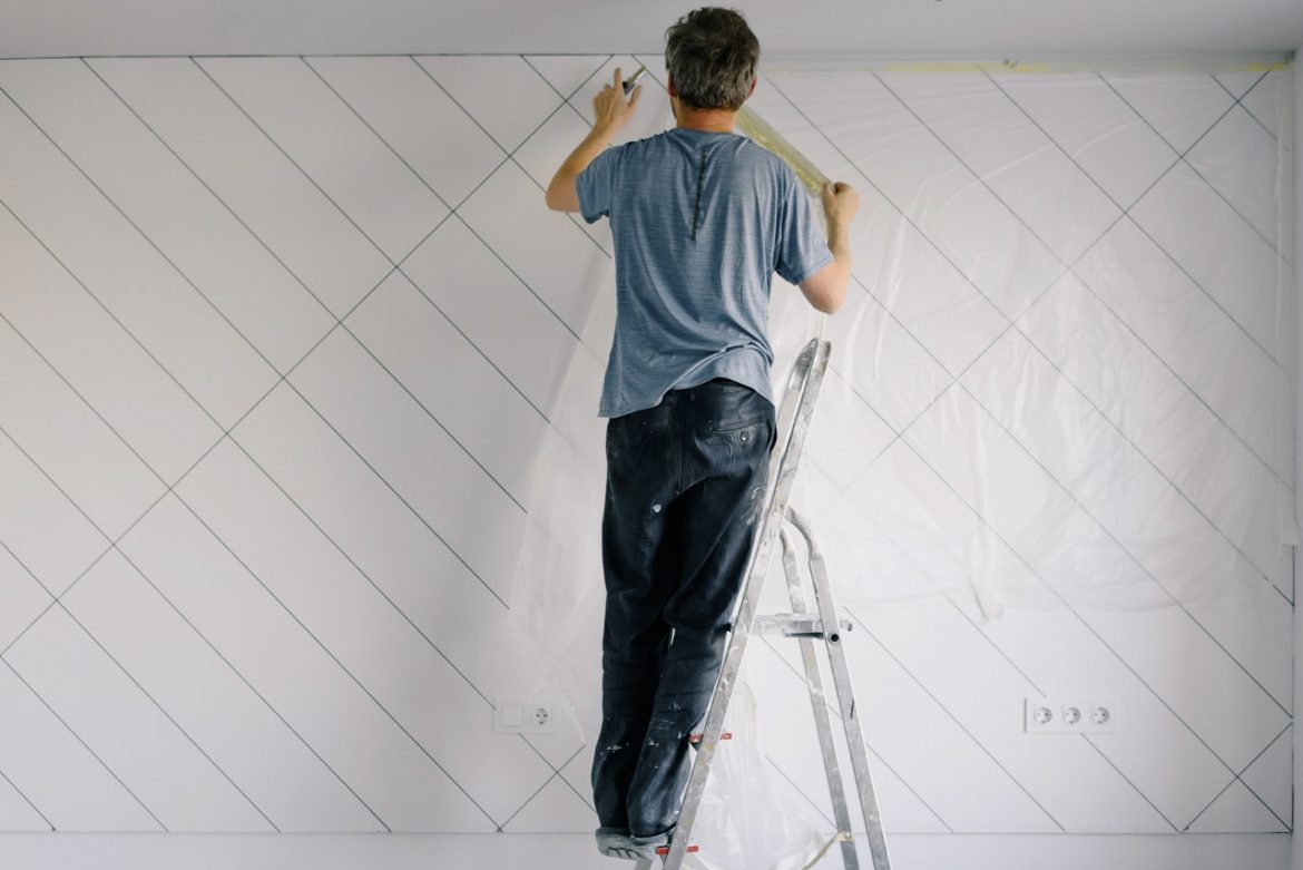 A man on a ladder painting a wall.