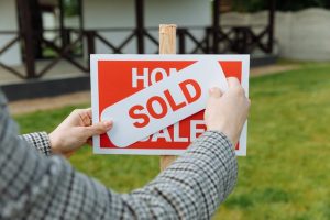 A person placing a sold sticker on a for sale sign in front of a house