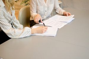 Two women sitting at a desk in white shirts with black details