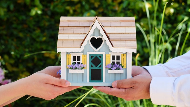 Persons holding a miniature house.