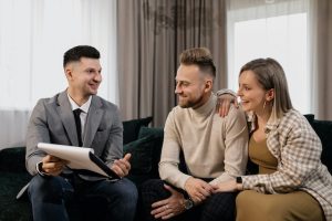 Two people sitting on the couch and talking to their real estate agent, who is one of the must-haves when house hunting