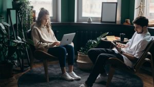 Couple sitting in chairs across from each other and looking at their smart devices