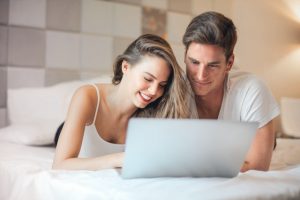 A happy couple lying in bed and looking at a laptop together