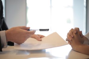 Person handing a contract and a pen to another person to sign